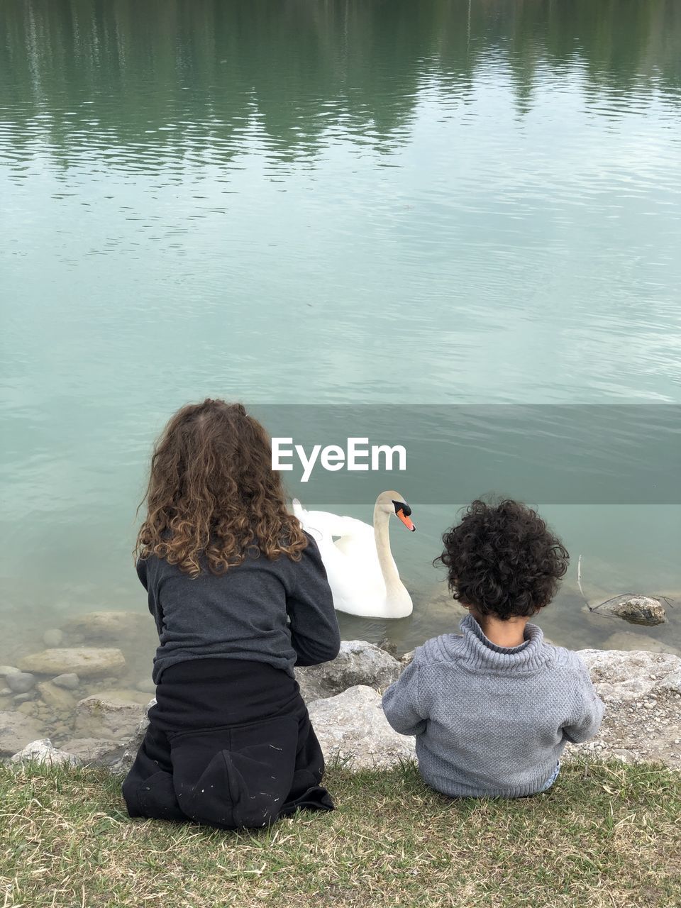 REAR VIEW OF WOMAN SITTING ON LAKE