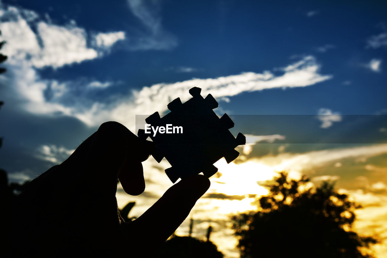 Cropped hand of person holding jigsaw piece against sky