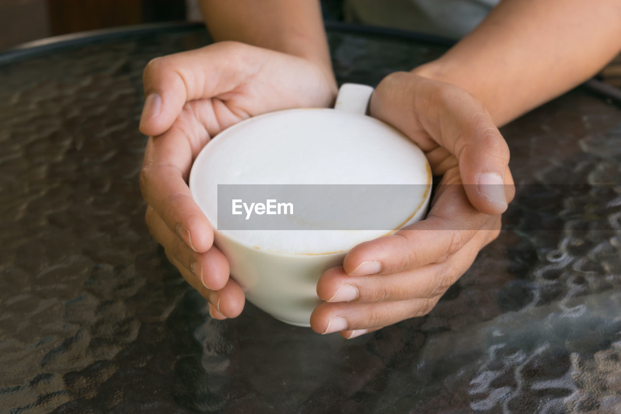 Cropped image of person holding frothy drink at table