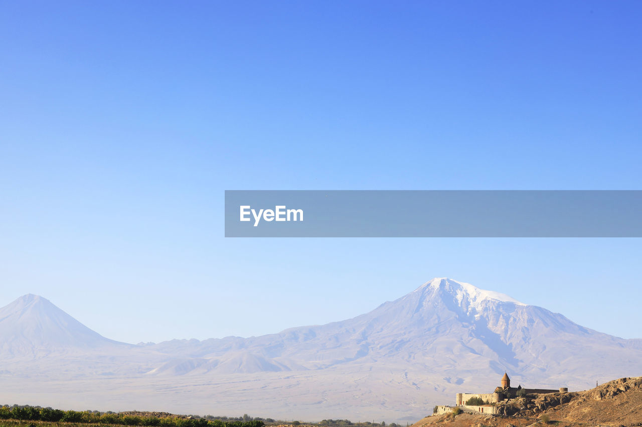 Scenic view of built structure against snowcapped mountain and sky