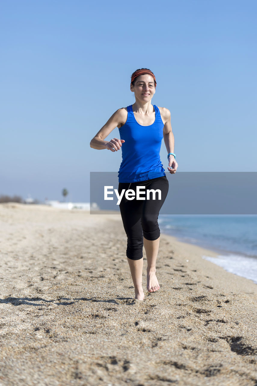 land, exercising, beach, sports, one person, sea, lifestyles, adult, nature, sports clothing, clothing, full length, sky, running, water, jogging, blue, leisure activity, vitality, motion, sand, person, front view, day, sports training, wellbeing, women, athlete, clear sky, copy space, sunlight, young adult, standing, outdoors, portrait, relaxation, sunny, determination, holiday, activity, vacation, summer, smiling, athleticism, human leg, casual clothing, trip, endurance, horizon over water, muscular build