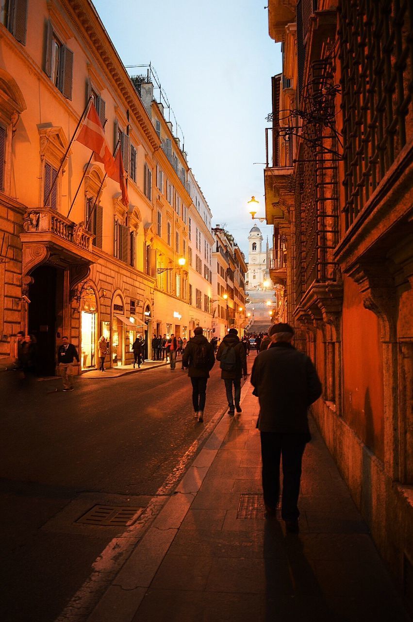 People walking on sidewalk by building in city at dusk