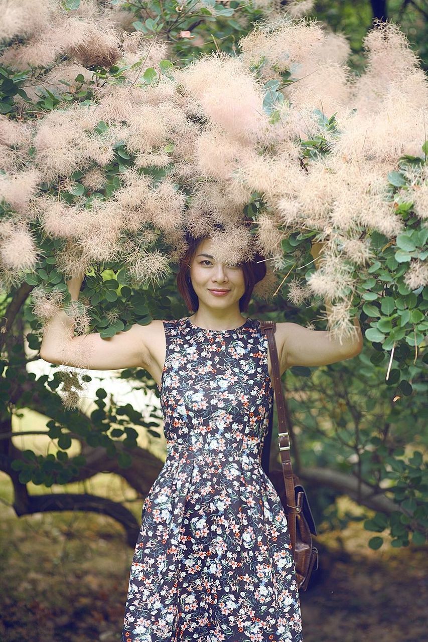 Portrait of smiling young woman touching tree