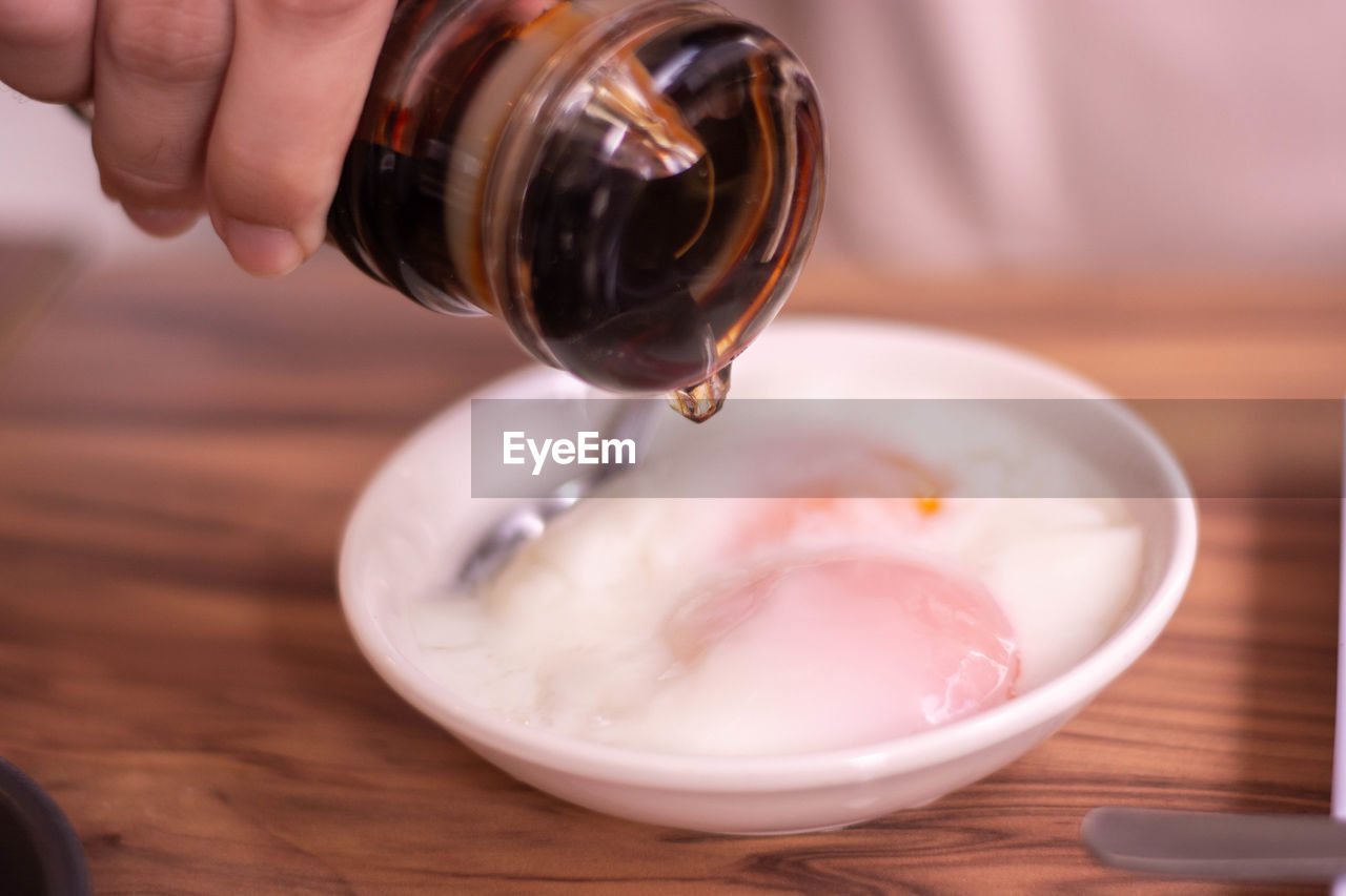 food and drink, hand, pouring, food, one person, indoors, wood, close-up, holding, bottle, household equipment, freshness, drink, refreshment, focus on foreground, adult, produce, lifestyles, breakfast, meal, motion, table, making, wellbeing, kitchen utensil