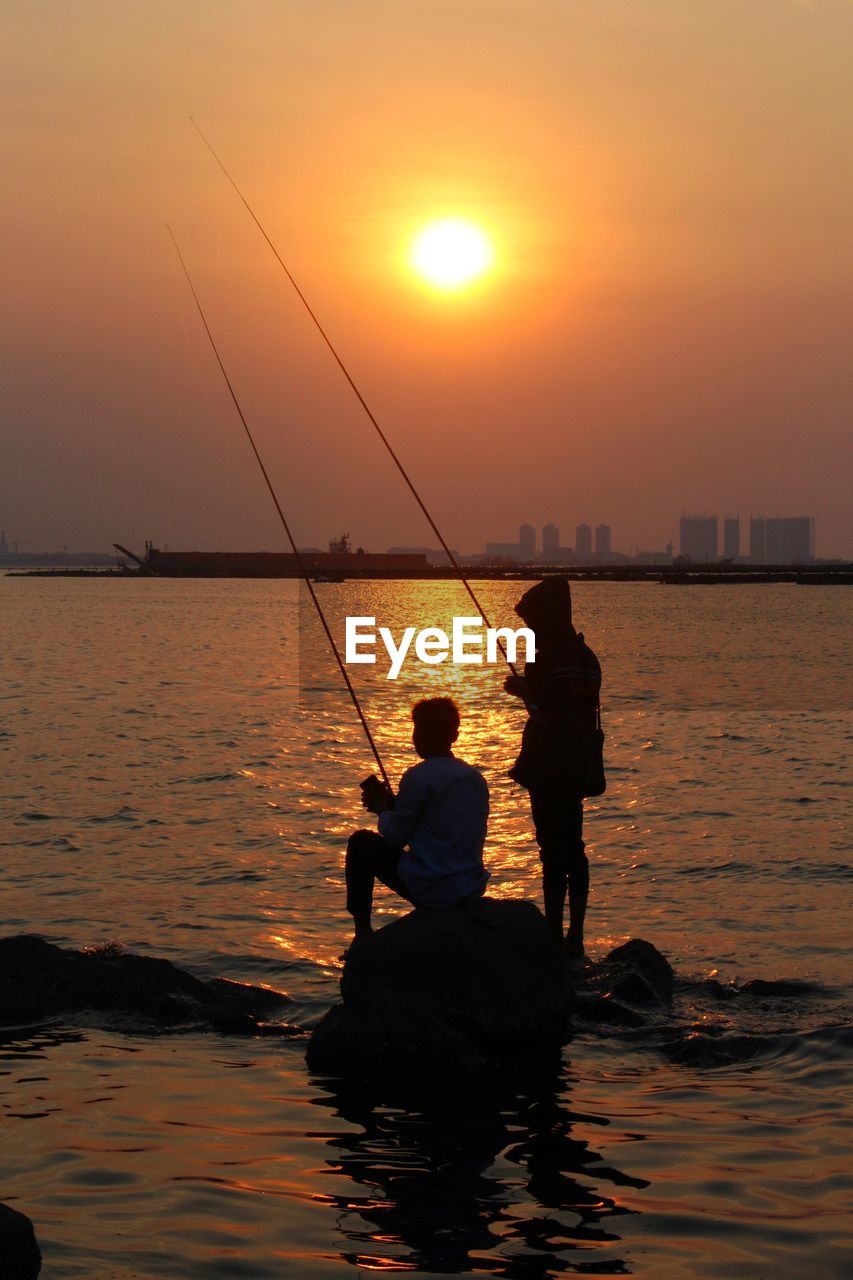 rear view of man fishing in sea against sky during sunset