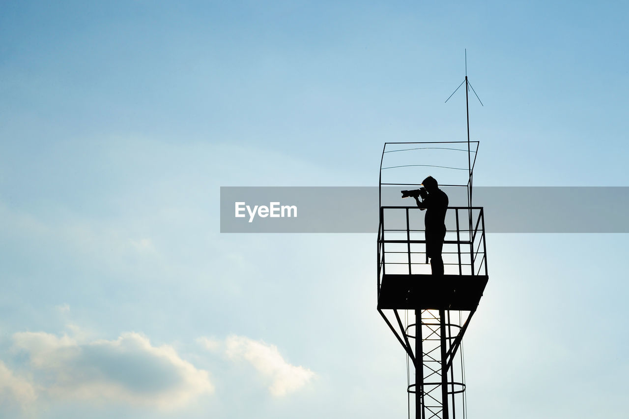 Low angle view of silhouette man standing in lookout tower against sky