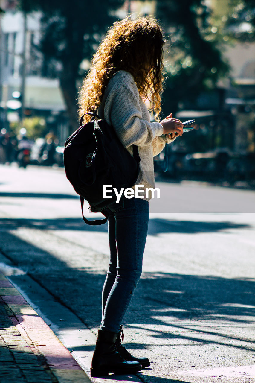 FULL LENGTH OF YOUNG WOMAN USING PHONE ON STREET