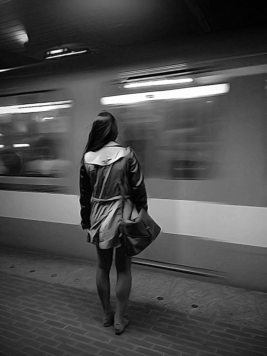 REAR VIEW OF WOMAN STANDING ON TRAIN AT ILLUMINATED STATION