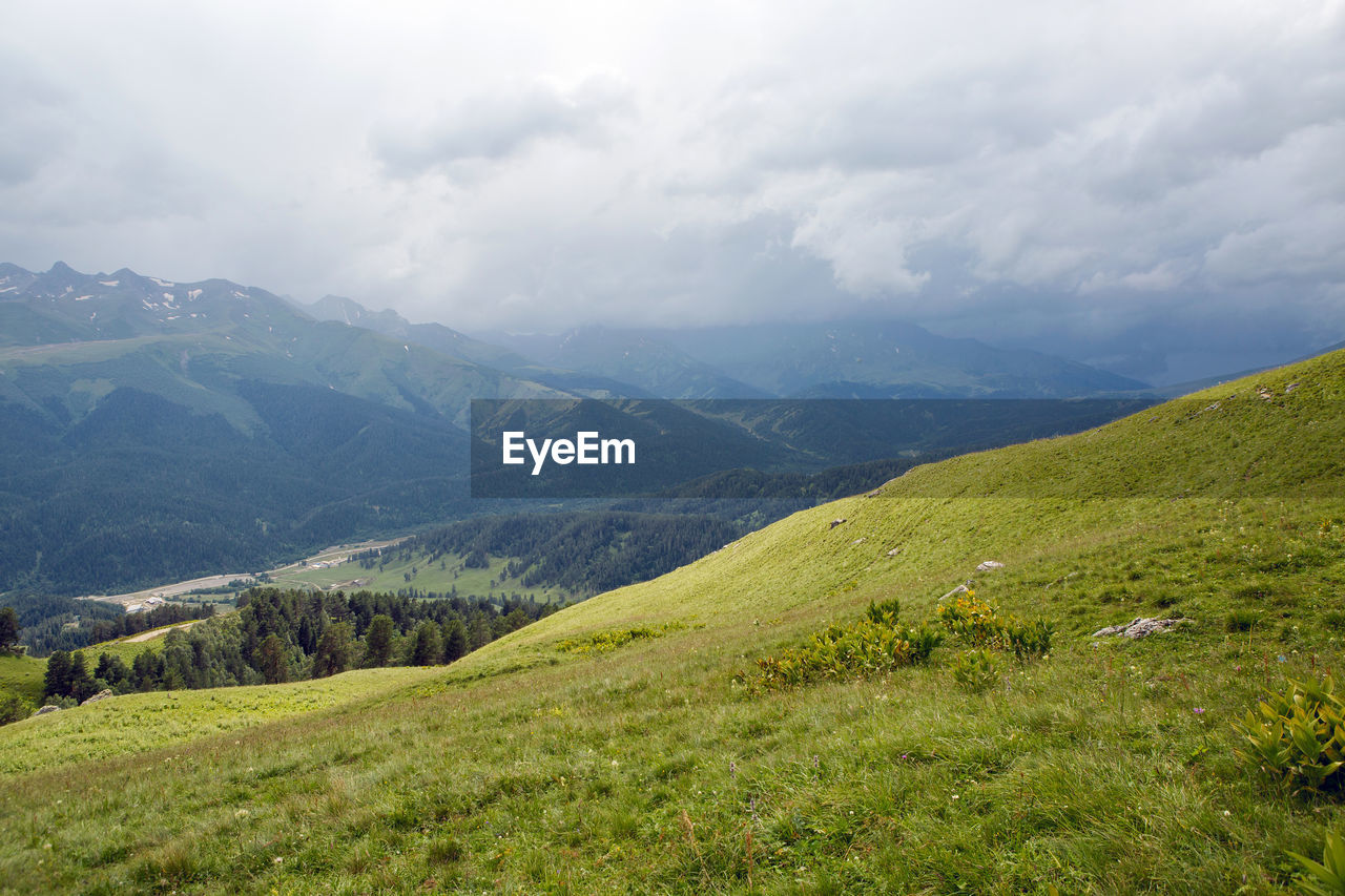 Green slope of a high mountain during a thunderstorm with clouds in the sky