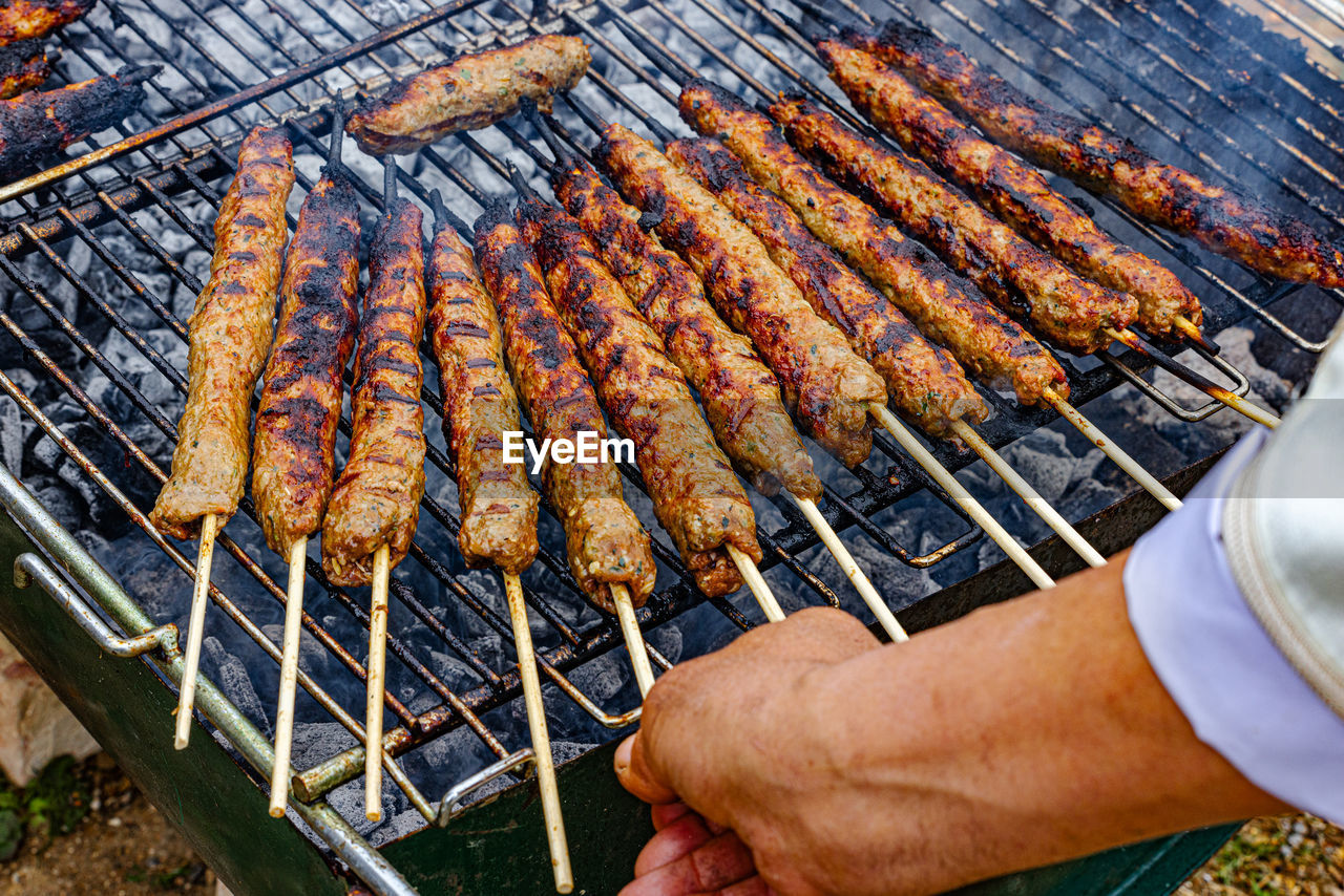 Cropped hand of man preparing kofta meat on barbecue grill