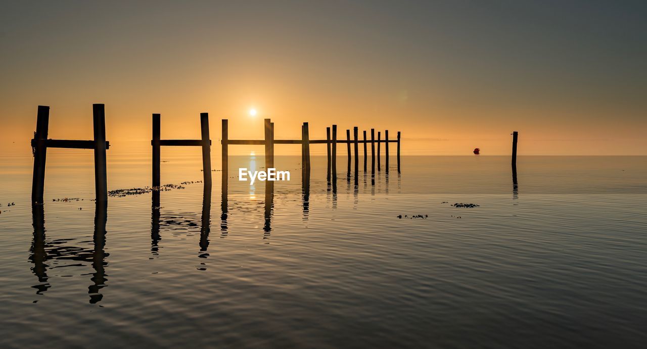 WOODEN POSTS IN LAKE DURING SUNSET