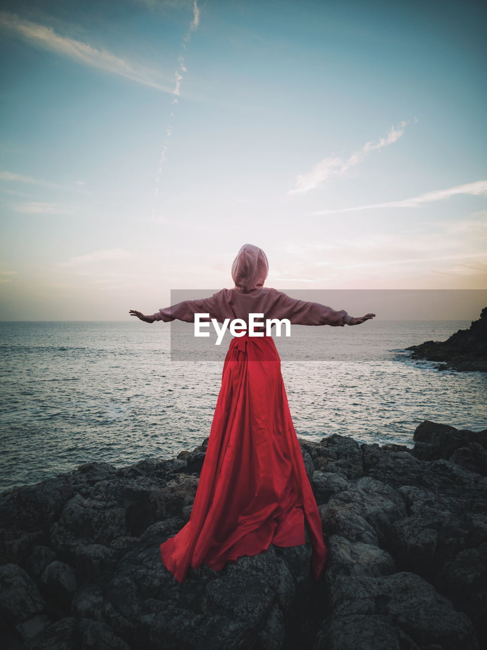 Rear view of girl with arms outstretched standing on rock at beach during sunset