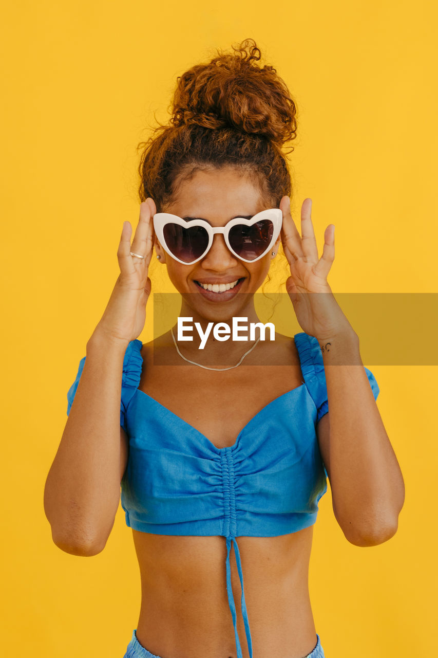 Smiling woman wearing heart shape sunglasses against yellow background