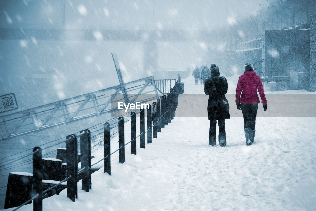 Rear view of people walking on snow covered bridge during winter