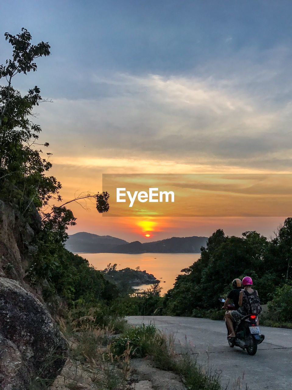 MAN CYCLING ON ROAD AGAINST SKY AT SUNSET