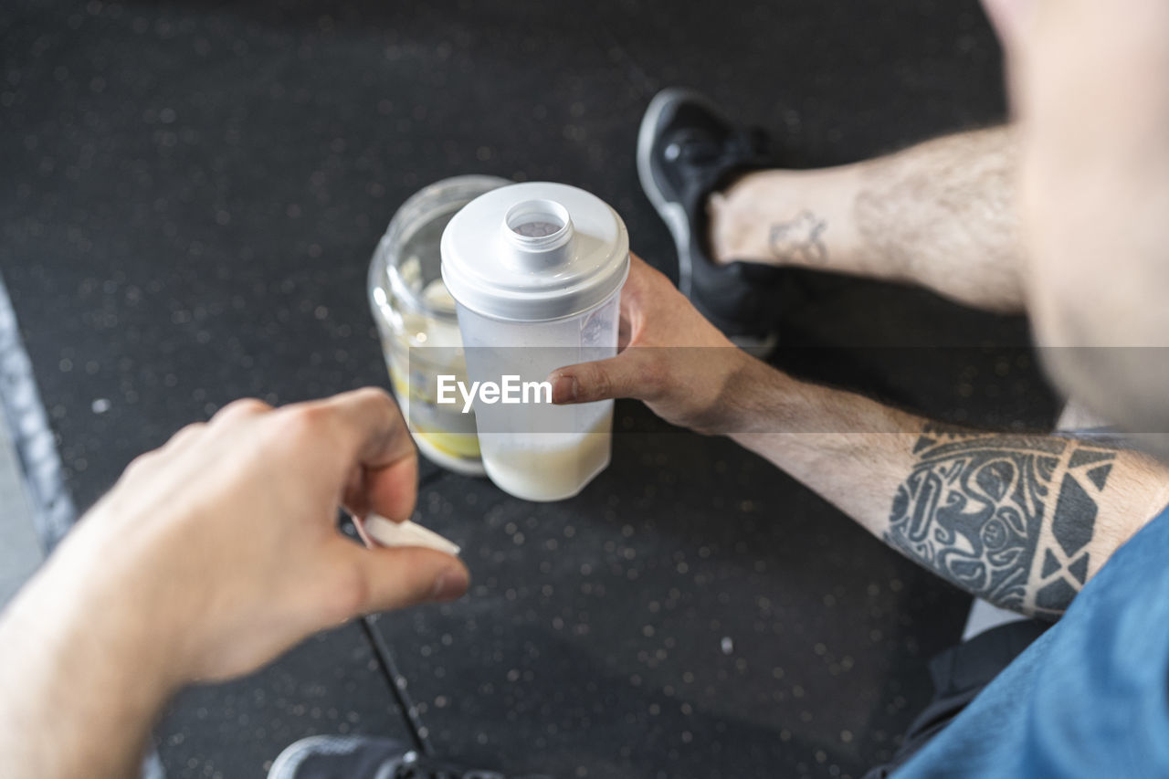 Close-up of sportsman holding protein shake while sitting in gym