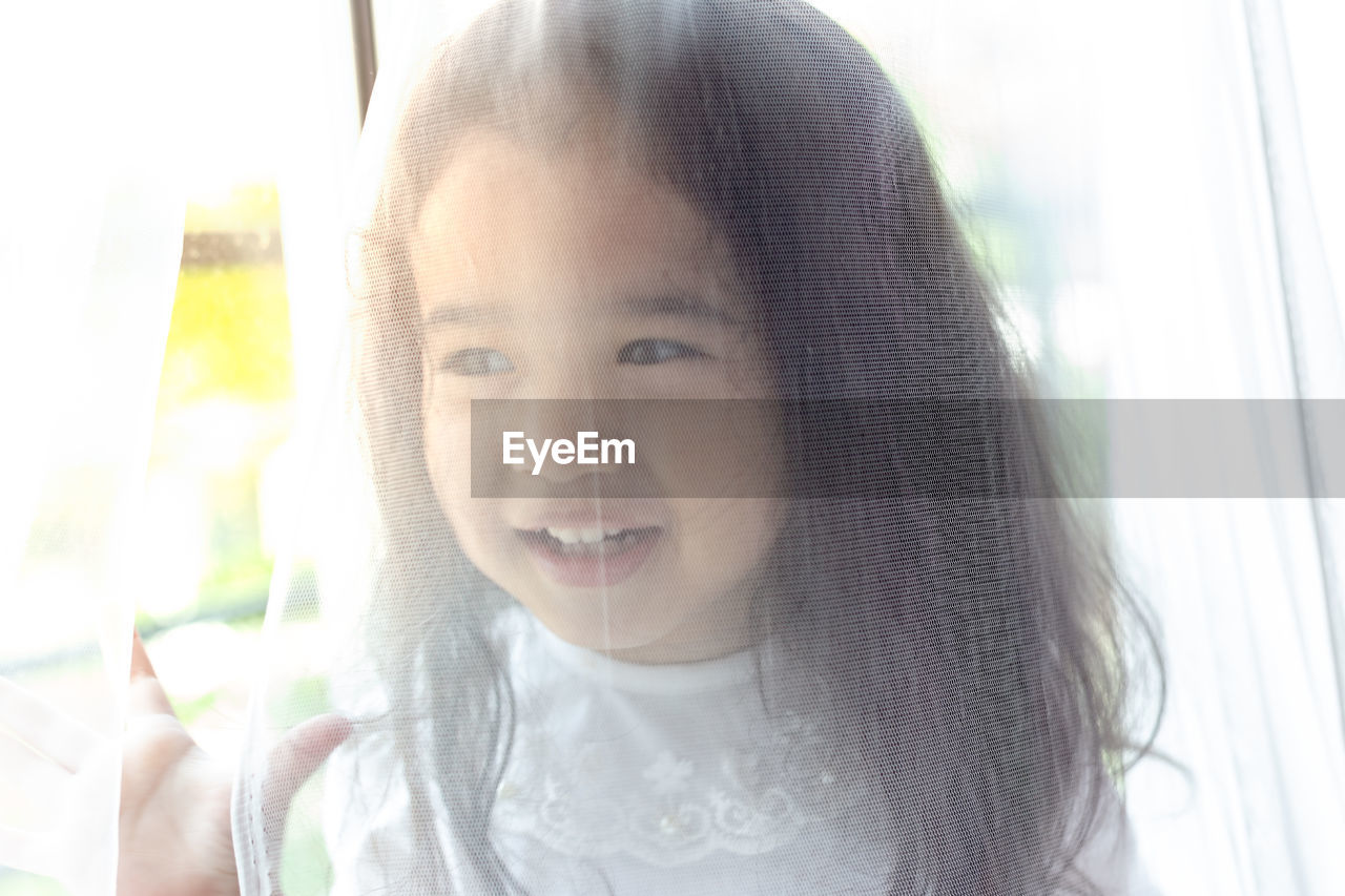 Close-up of cute smiling girl seen through transparent textile