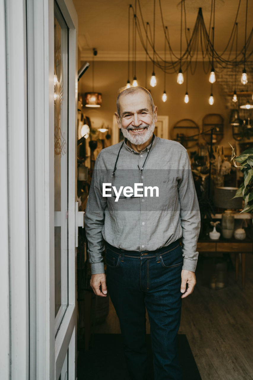 Smiling senior male entrepreneur standing near door of home interior store