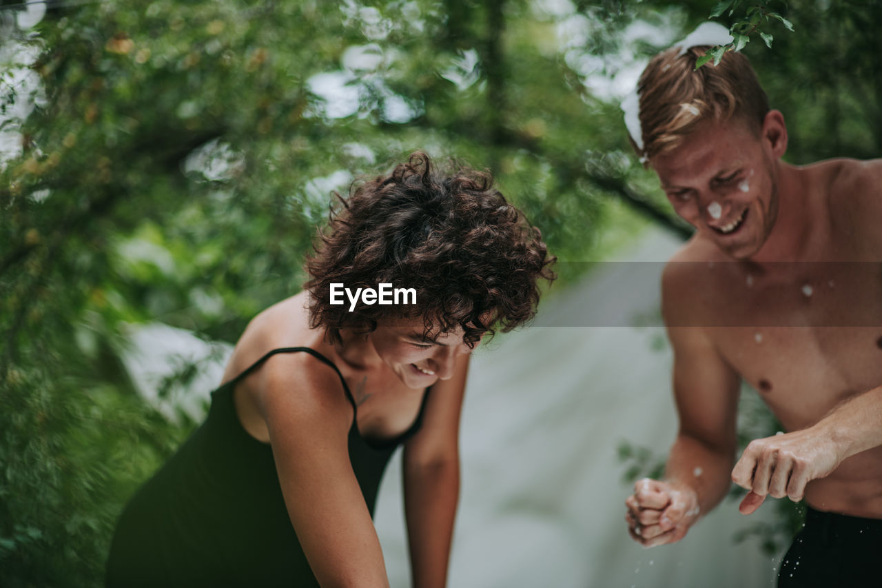 Midsection of shirtless young woman against trees