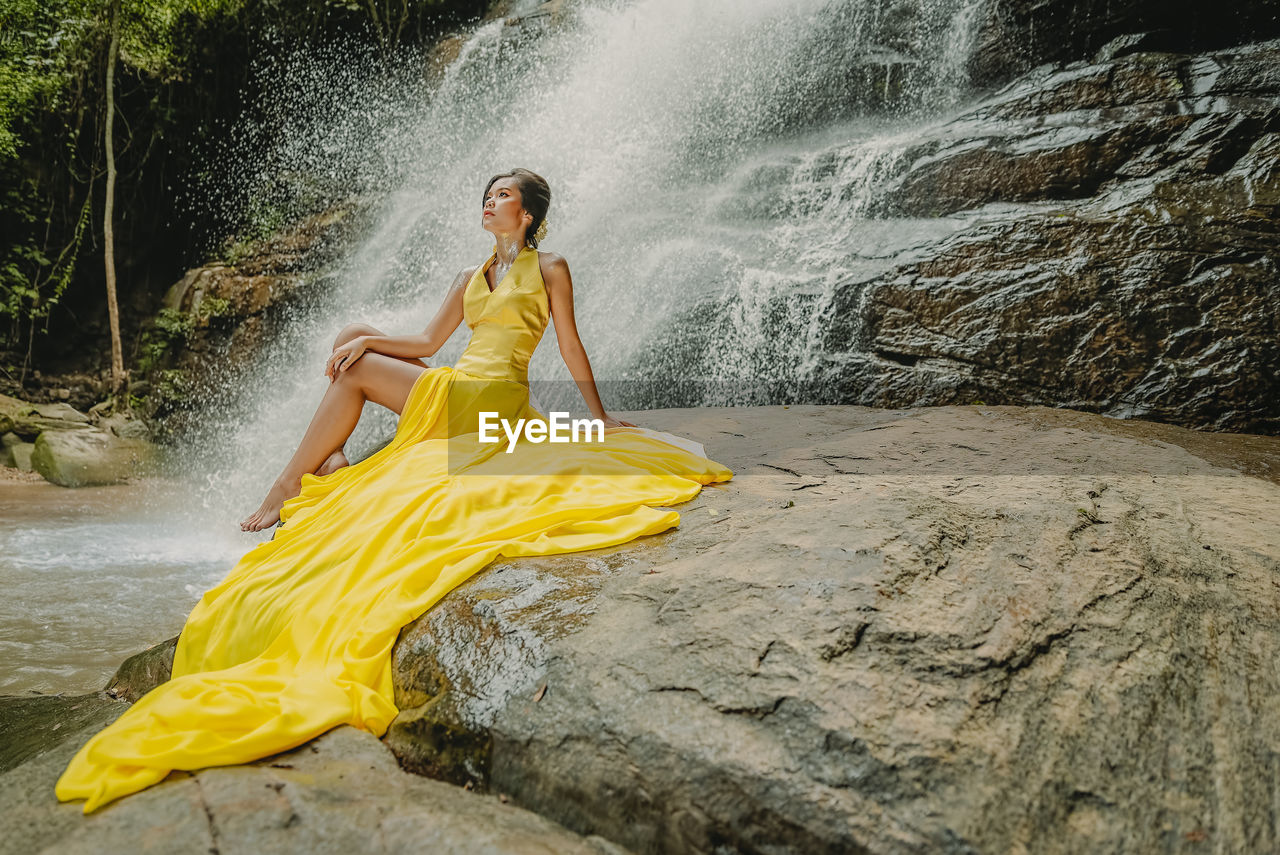 Full length of woman sitting against waterfall