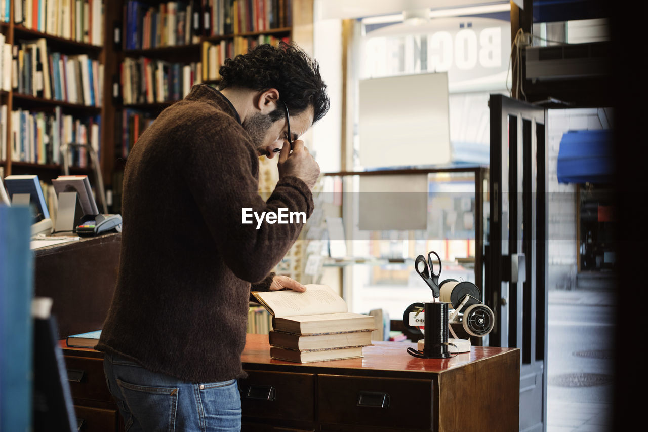 Owner holding eyeglasses while reading book in library