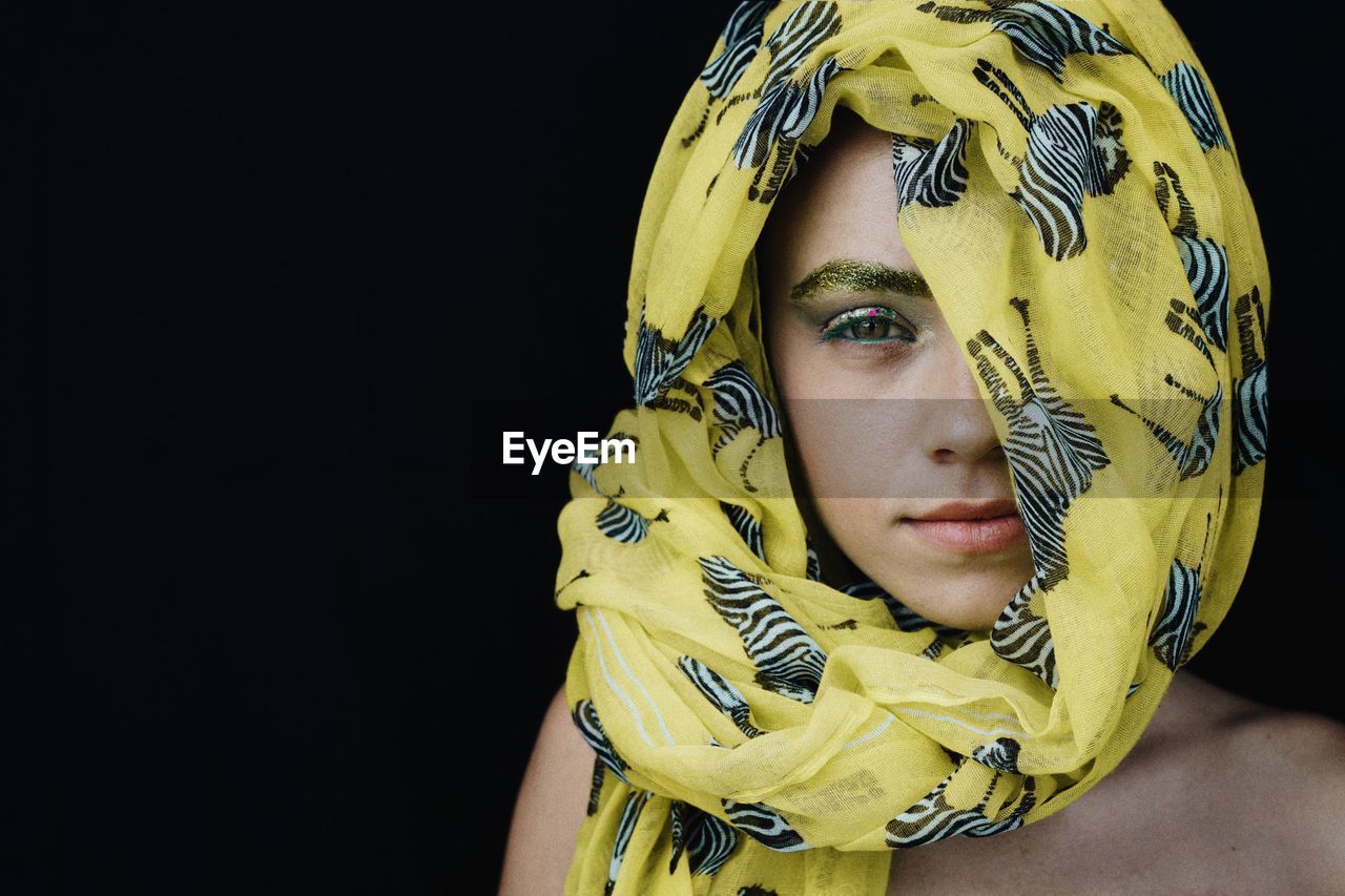 Portrait of young woman wearing yellow headscarf against black background