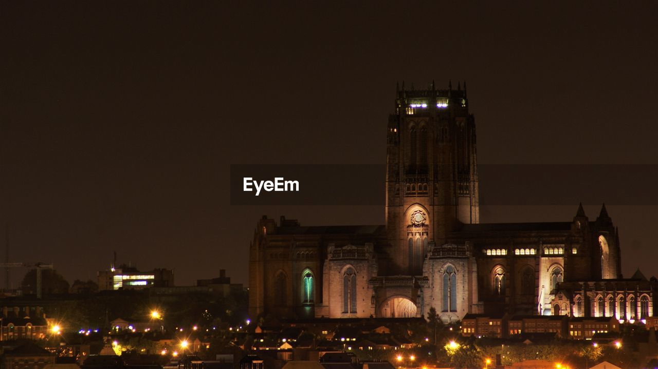 Illuminated anglican cathedral amidst buildings against clear sky at night