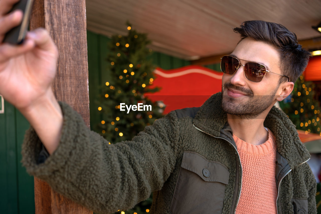 portrait of young man wearing sunglasses while standing against wall