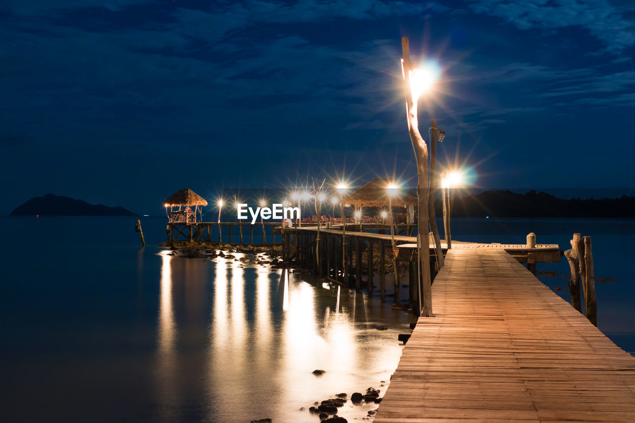 Illuminated pier on sea against sky at night