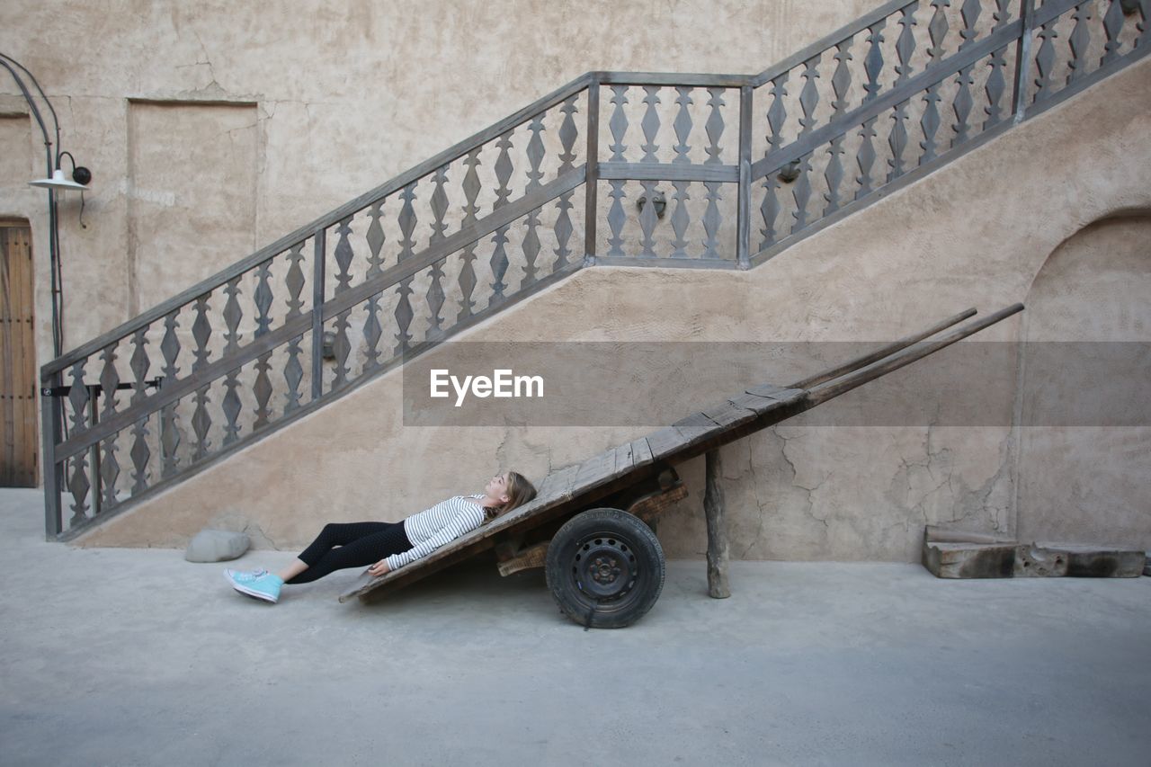 Woman lying on cart against building