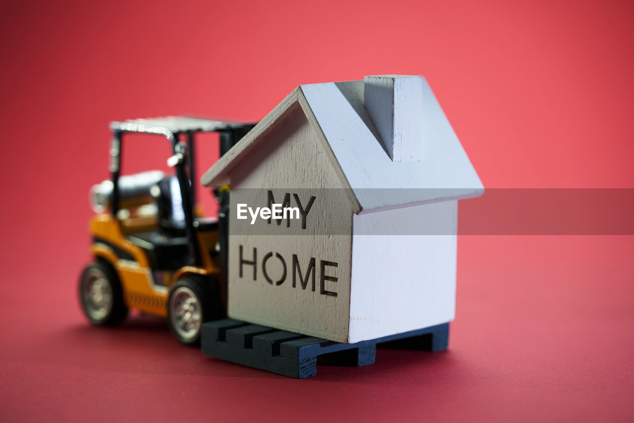 House moving concept with miniature forklift and model house on red background