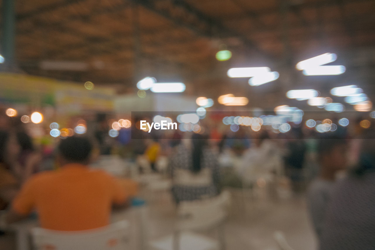 DEFOCUSED IMAGE OF PEOPLE STANDING ON ILLUMINATED STREET IN CITY AT NIGHT