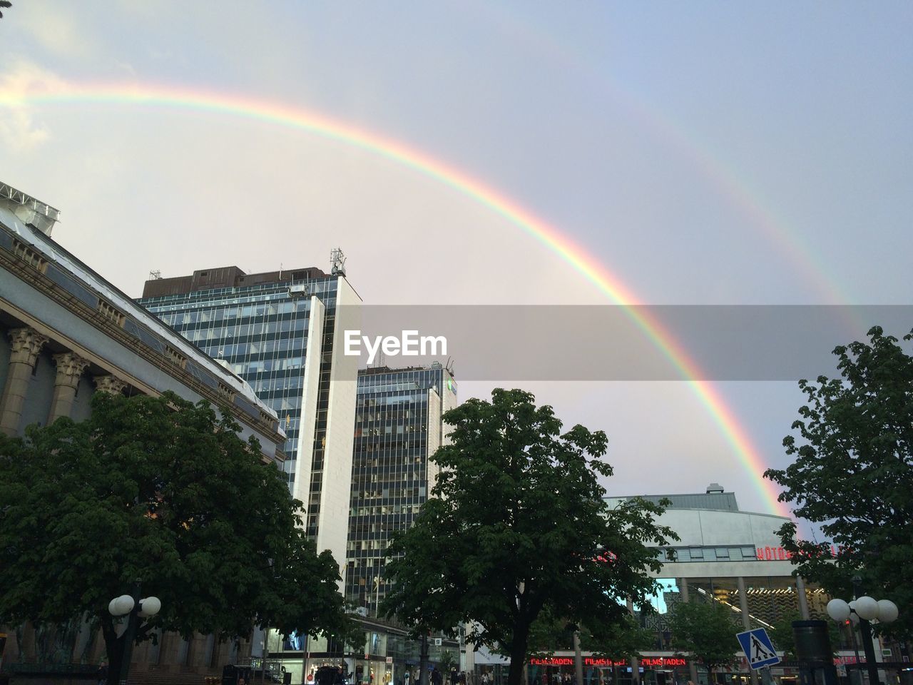 Low angle view of rainbow over modern buildings against sky in city