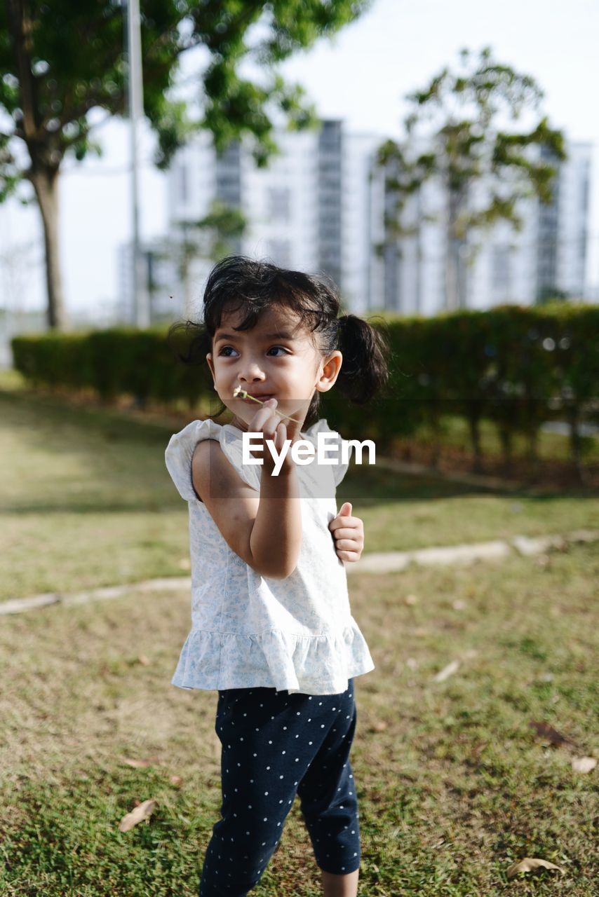 Portrait of cute girl on field at city garden 