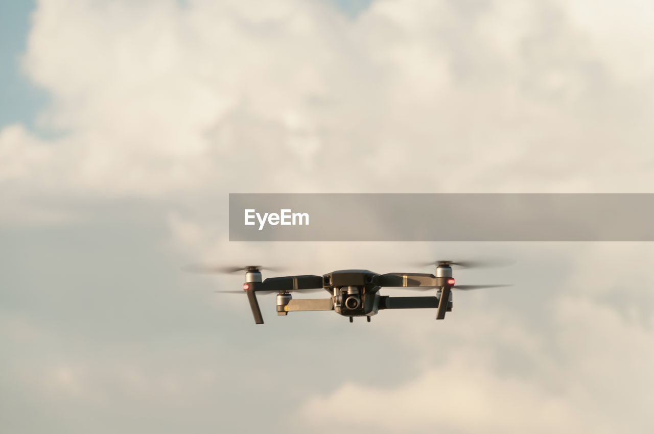 Low angle view of drone flying against cloudy sky