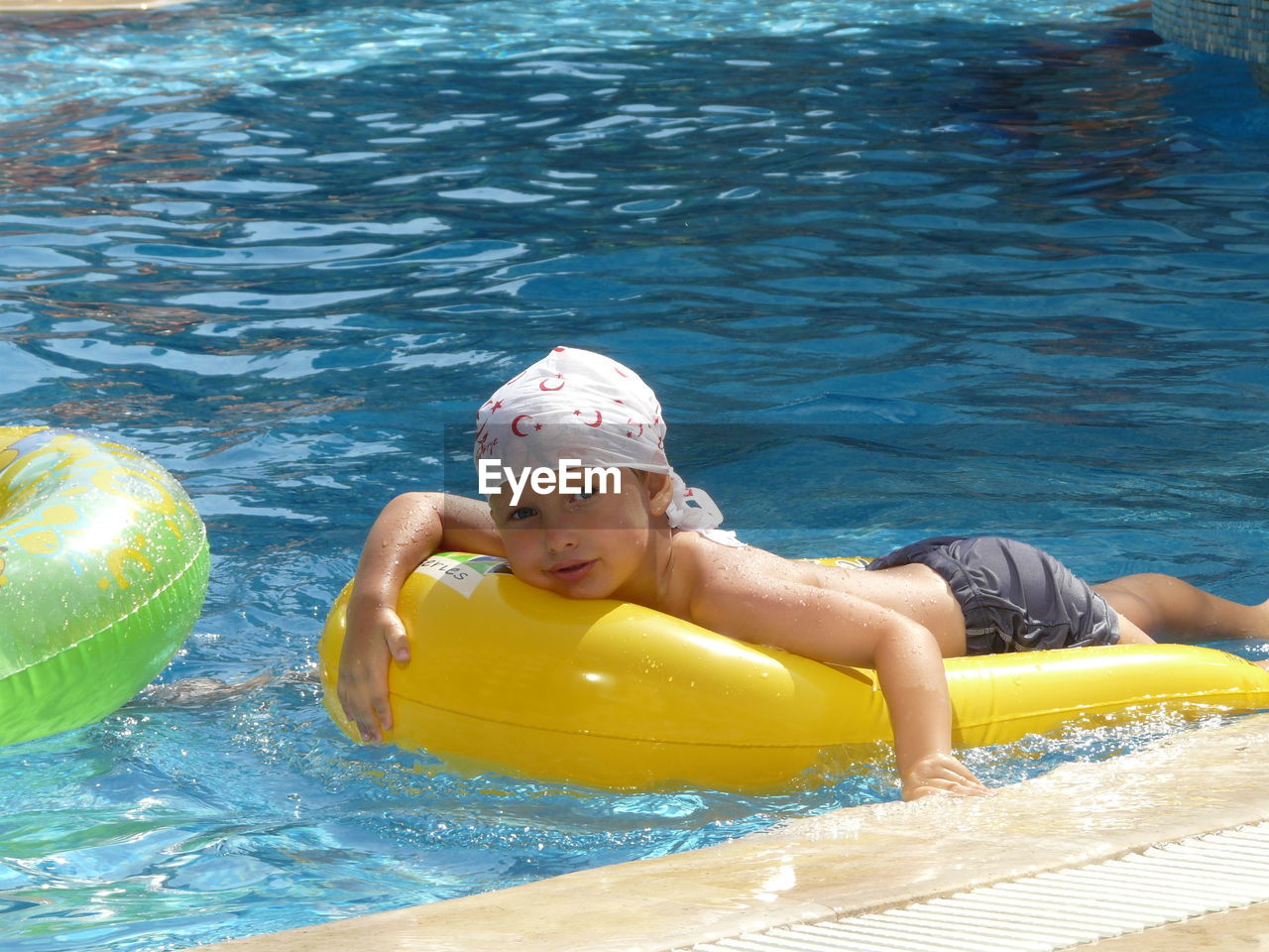 Portrait of shirtless boy floating on inflatable ring in swimming pool