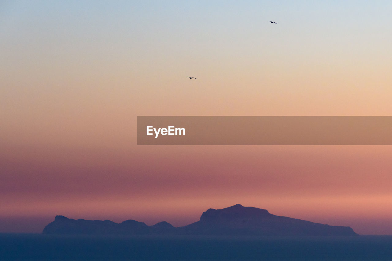 Silhouette isle of capri over sea against sky during sunset