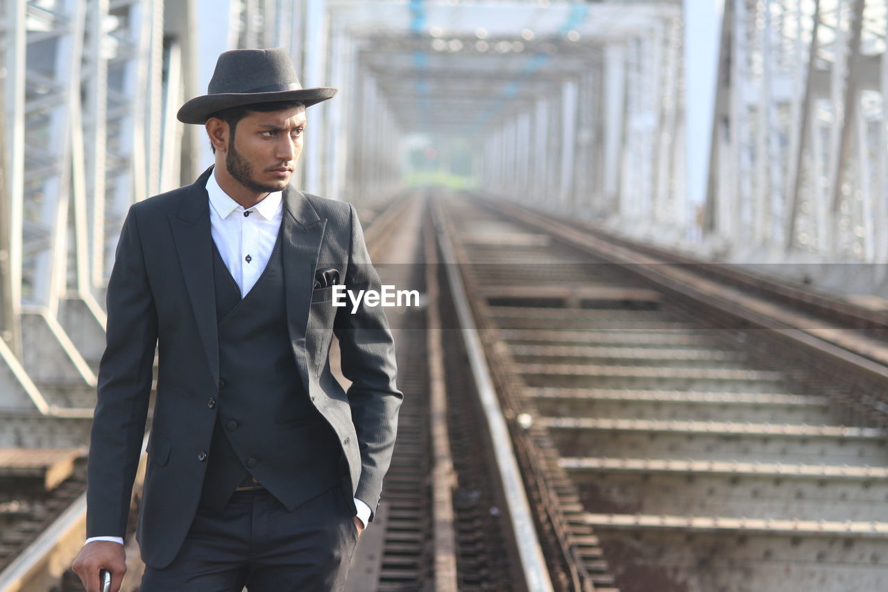 Man in suit looking away while standing at railway bridge