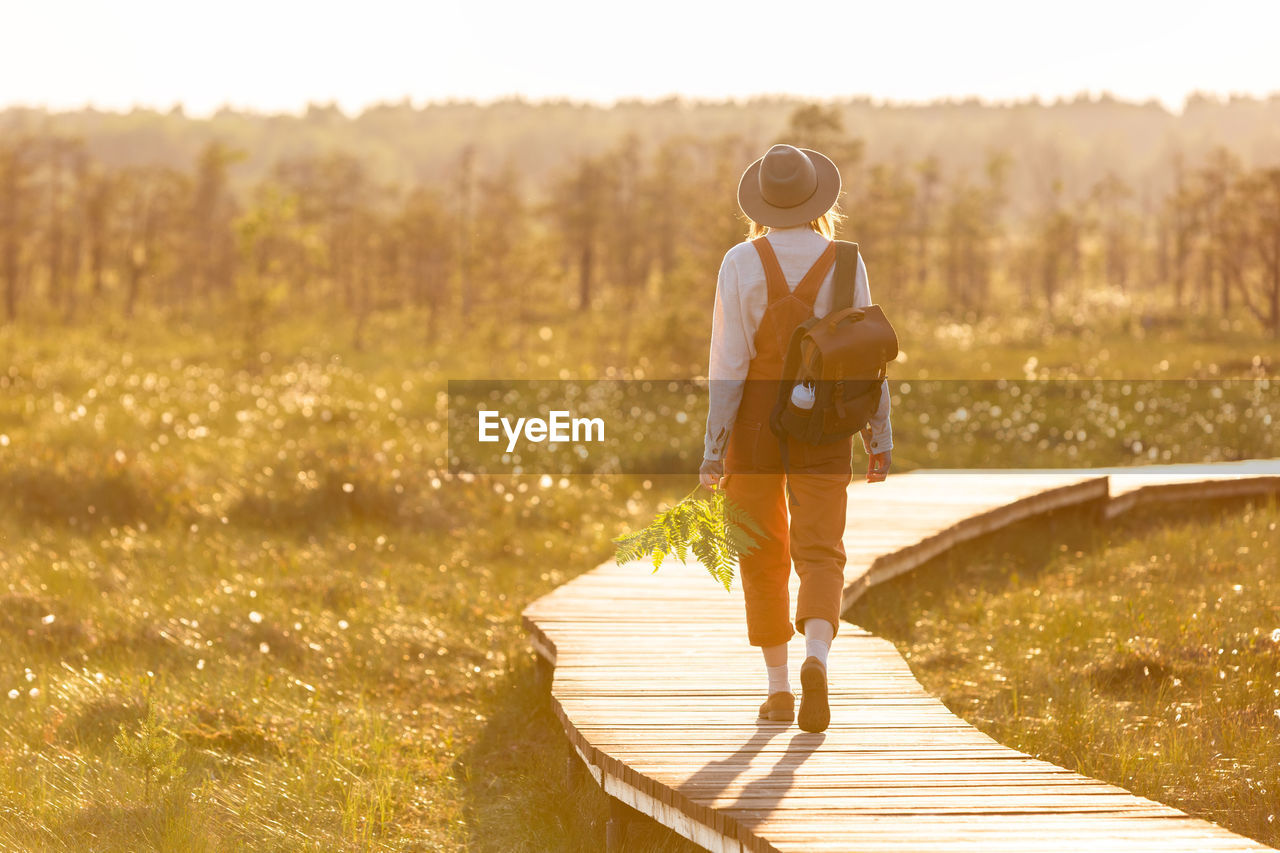 Naturalist woman botanist with backpack on ecological hiking trail in summer outdoors. 