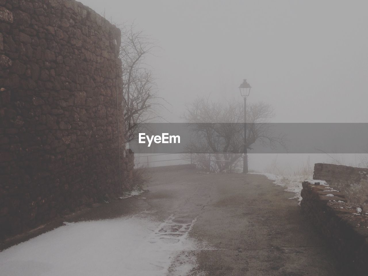 Snow on empty road by wall in foggy weather