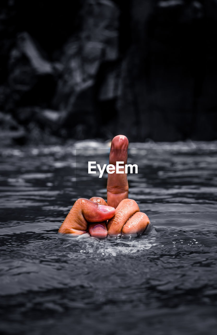 Close-up of person showing middle finger in water