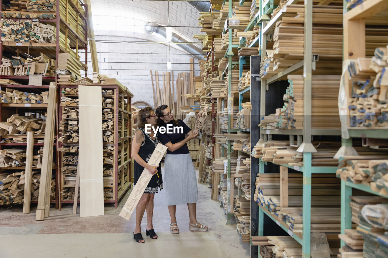 Women choosing ornate wood panel while standing in warehouse at factory
