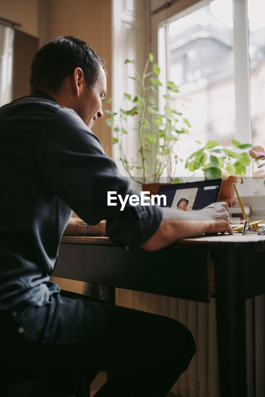 Male entrepreneur discussing with colleague on video call over laptop at home