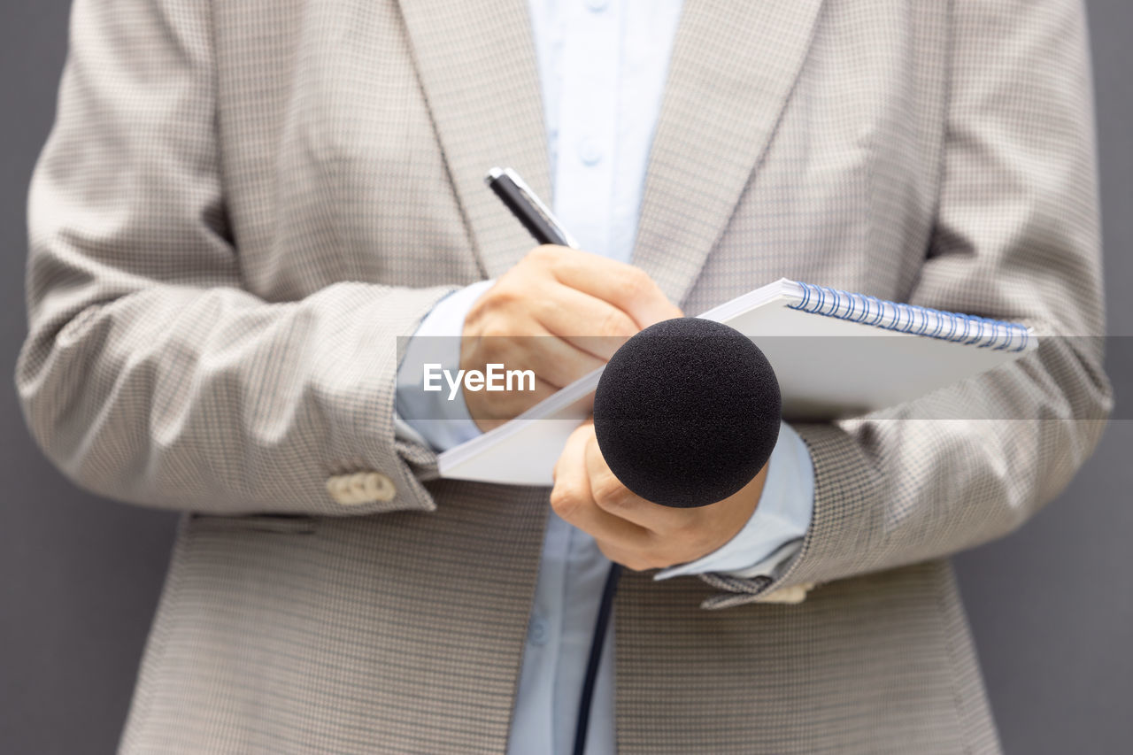 Female journalist at news conference or media event, writing notes, holding microphone