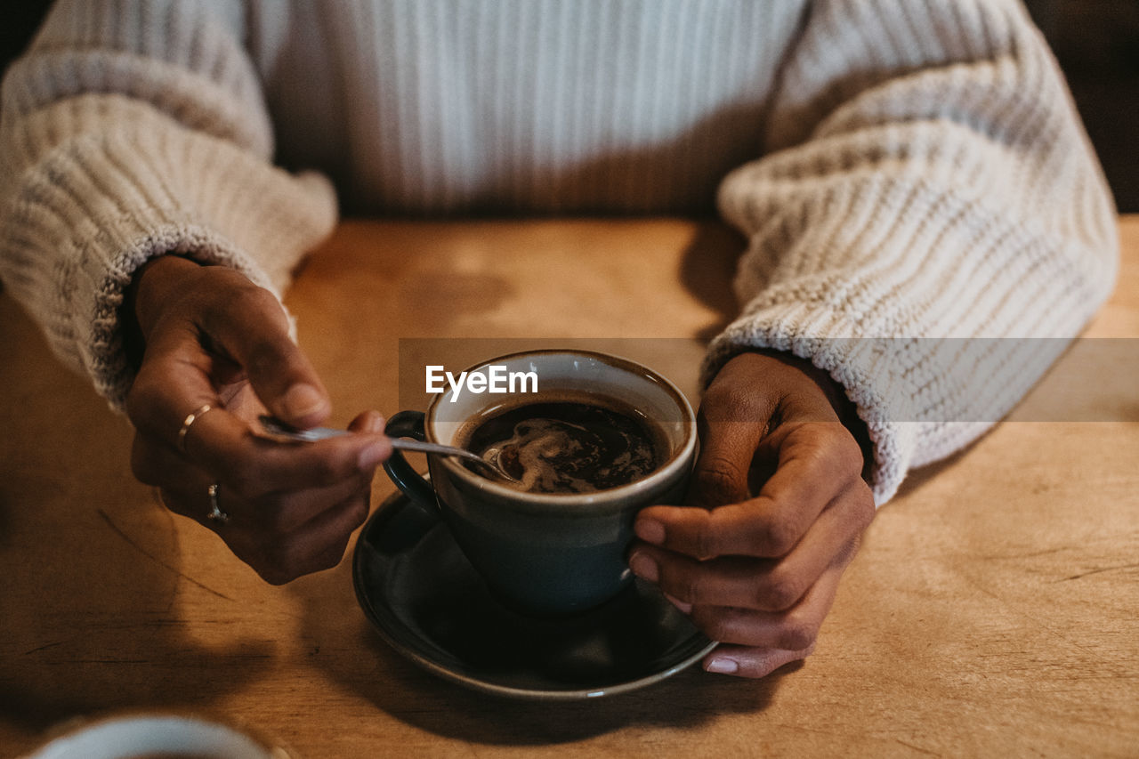 From above crop hands of unrecognizable female sitting at wooden table holding hot coffee in a rustic mug