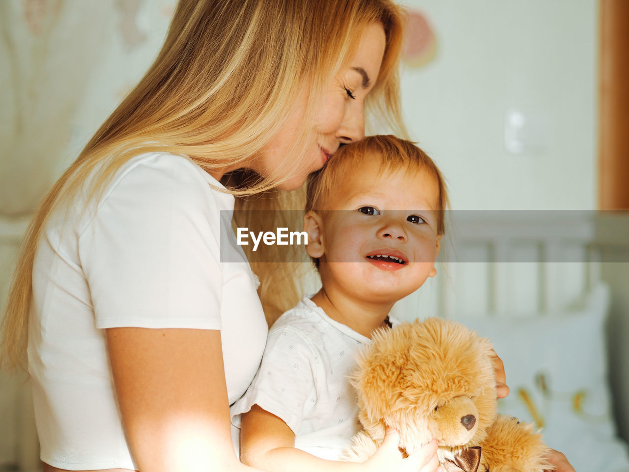 Young beautiful mother with long blond hair having fun with pretty baby boy at home