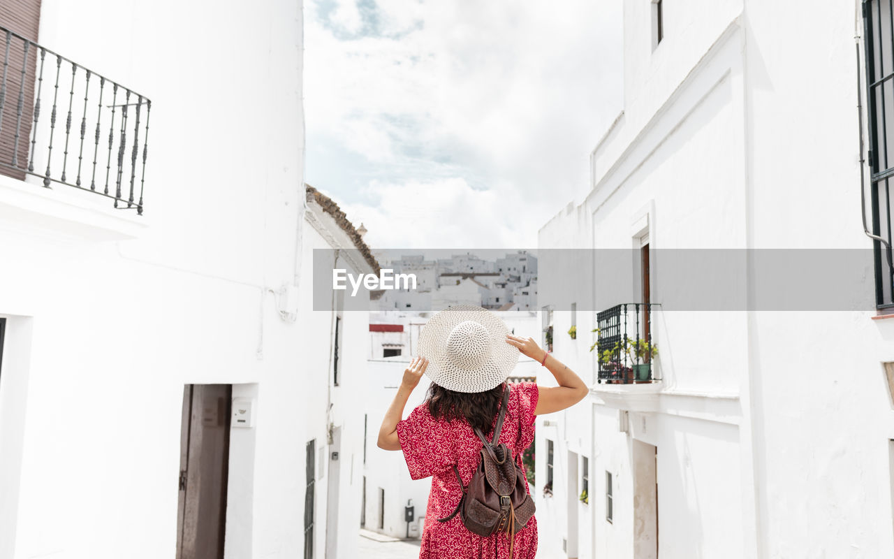 Back view of unrecognizable female tourist with raised arms on narrow street between old houses in greece