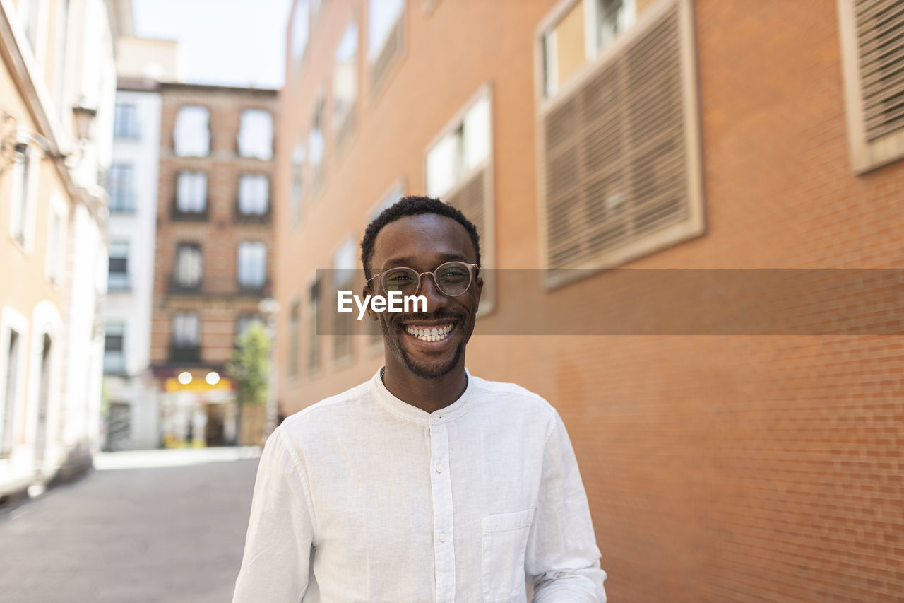 Young man in eyeglasses smiling in front of buildings