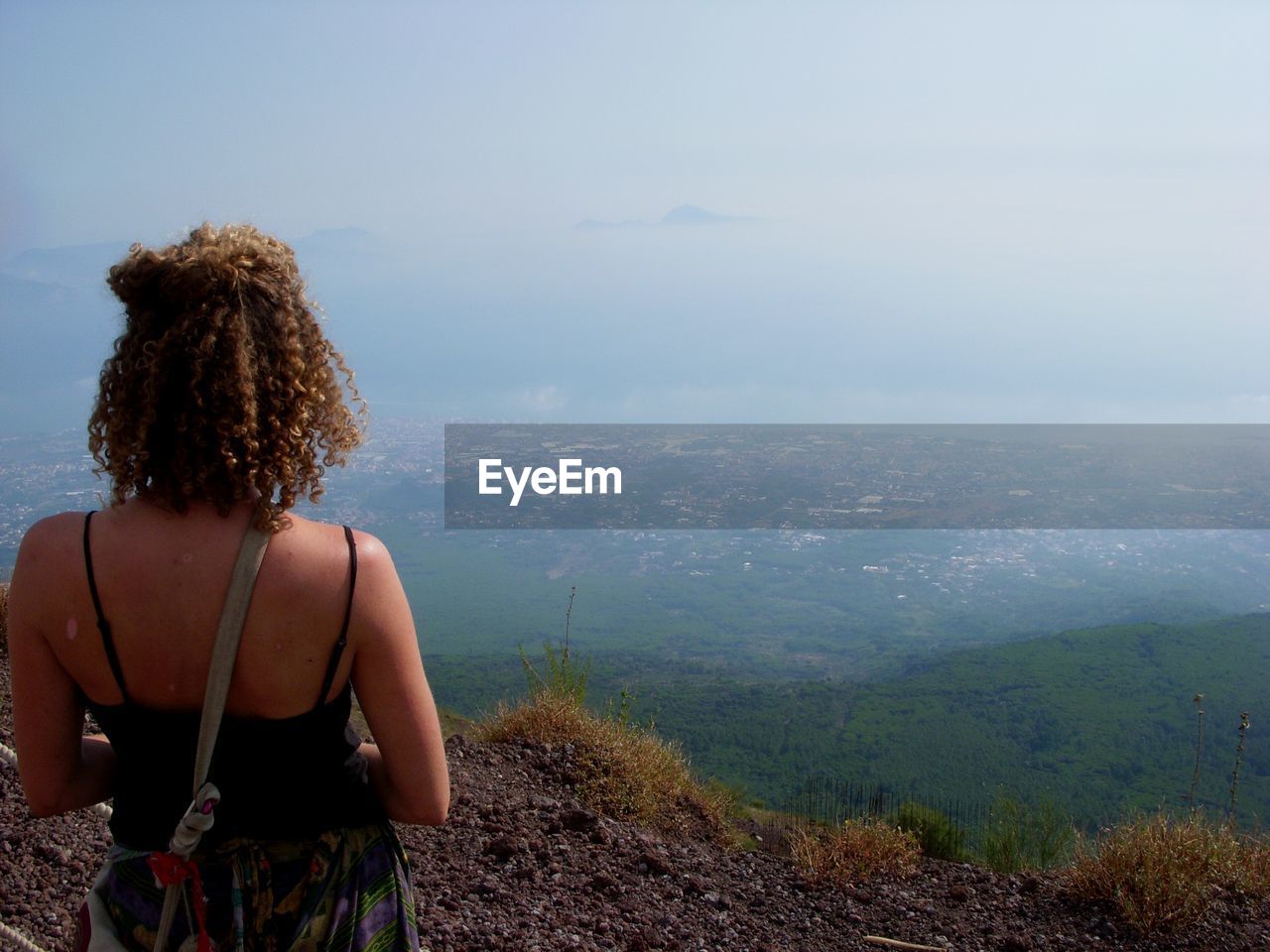 Woman with curly hair standing on cliff against mountains