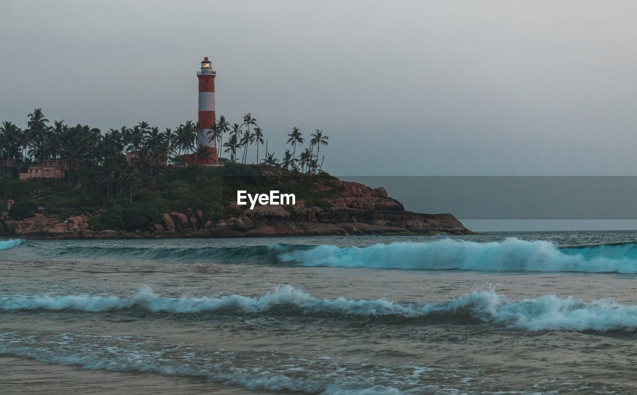 Lighthouse by sea against clear sky